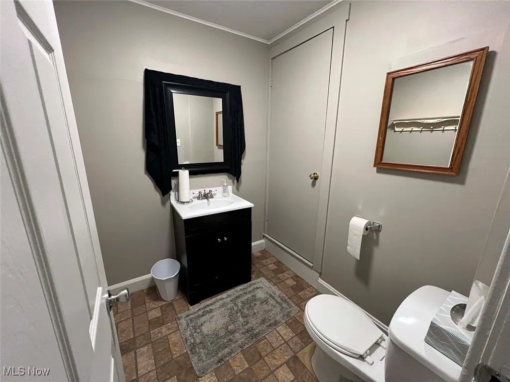 Bathroom with crown molding, vanity, baseboards, toilet, and stone finish floor