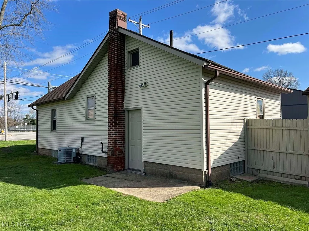 View of side of home featuring a yard, central air condition unit, a chimney, and fence