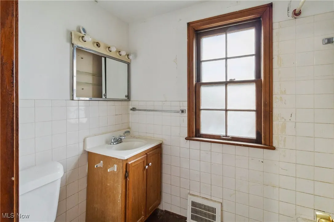 Half bath with visible vents, toilet, vanity, tile walls, and wainscoting