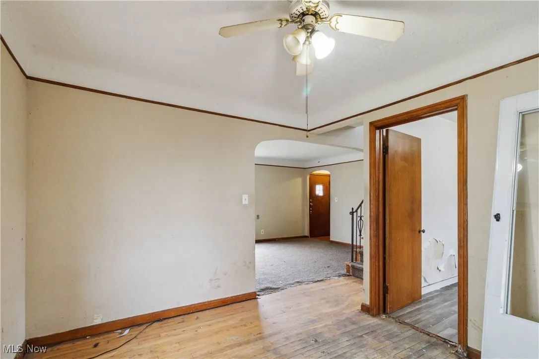 Unfurnished room featuring hardwood / wood-style flooring, arched walkways, ceiling fan, and crown molding