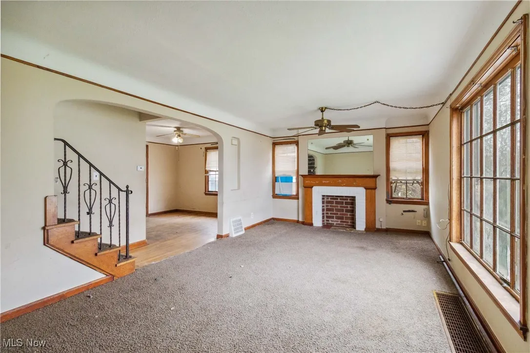 Unfurnished living room with arched walkways, carpet floors, and ceiling fan