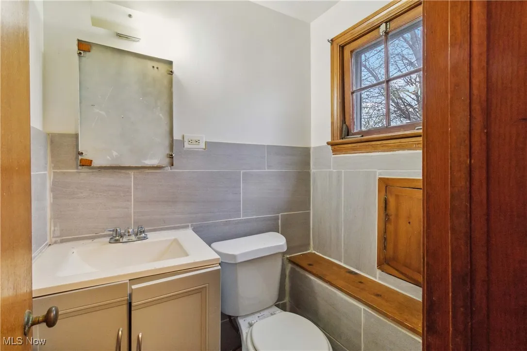 Bathroom with tile walls, wainscoting, vanity, and toilet