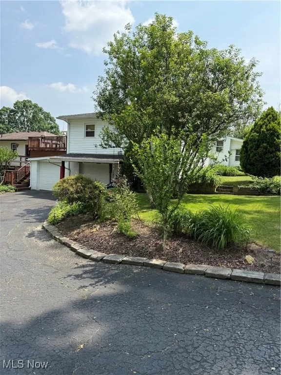 View of property hidden behind natural elements featuring an attached garage, asphalt driveway, and a front yard