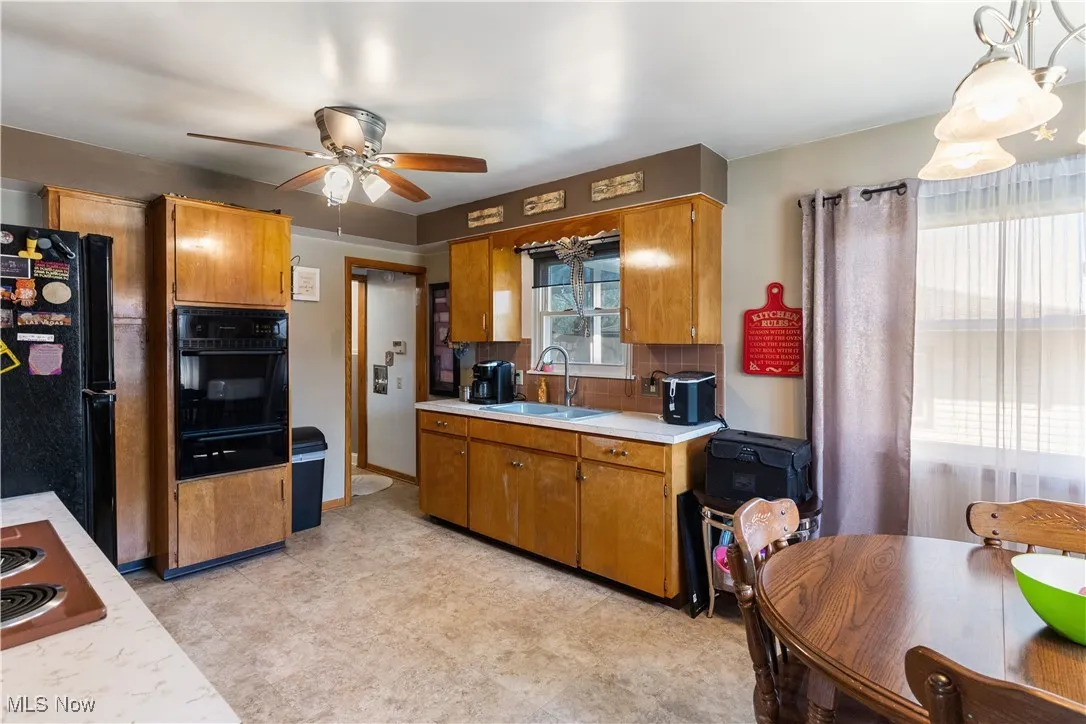 Kitchen featuring brown cabinets, light countertops, a ceiling fan, a sink, and black appliances