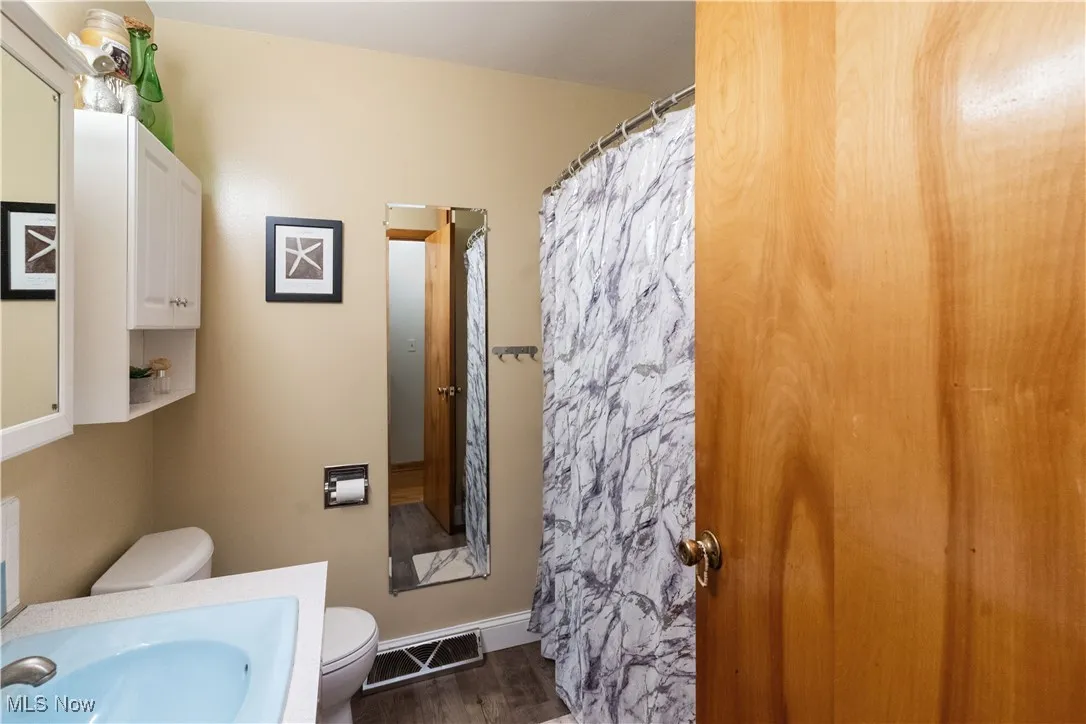 Full bathroom with wood finished floors, visible vents, toilet, vanity, and a shower with curtain