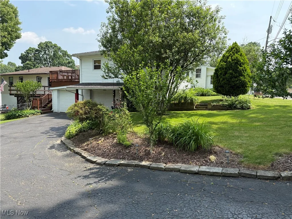 View of property hidden behind natural elements with driveway, a front lawn, and a garage