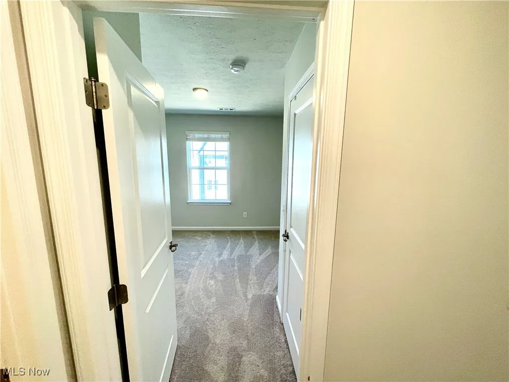 Corridor with baseboards, carpet flooring, and a textured ceiling