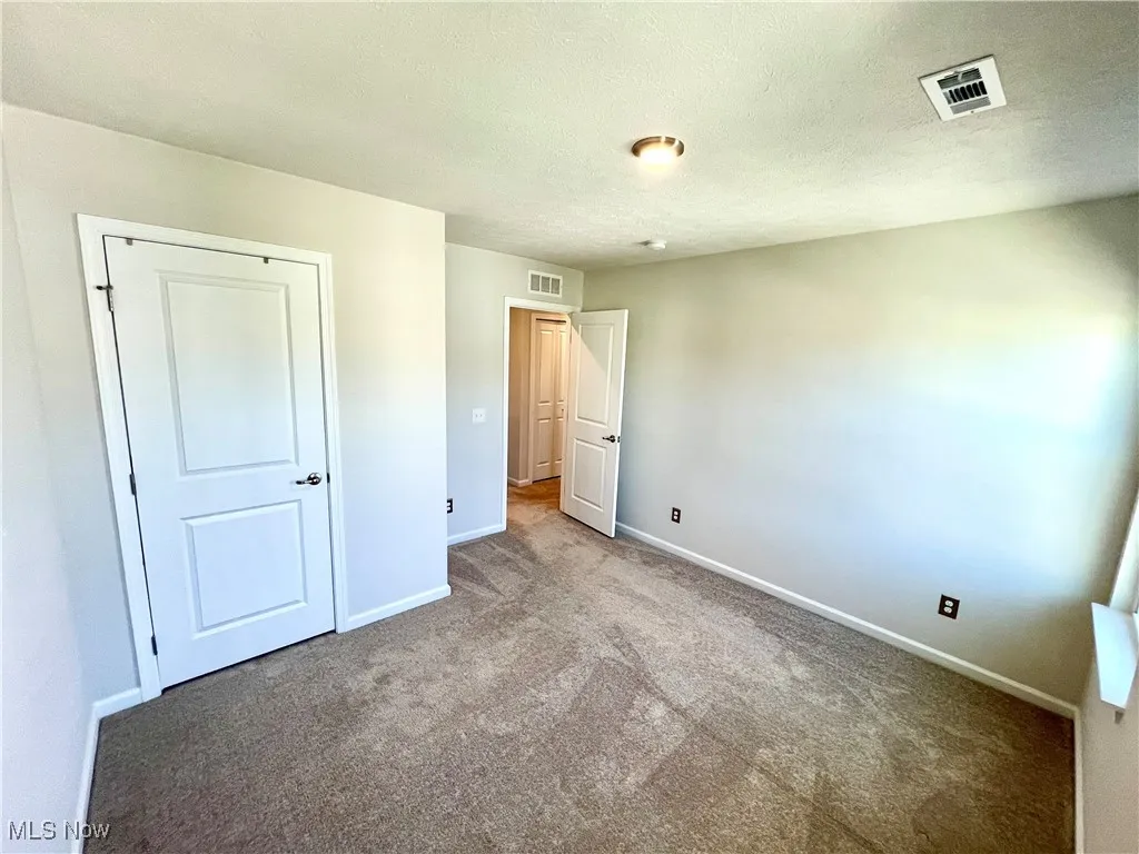 Unfurnished bedroom with a textured ceiling, carpet, visible vents, and baseboards