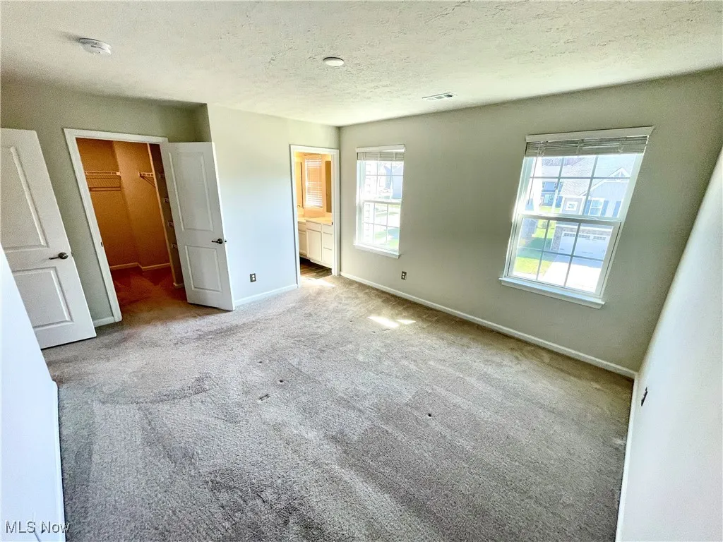 Unfurnished bedroom with a textured ceiling, a walk in closet, connected bathroom, baseboards, and carpet flooring