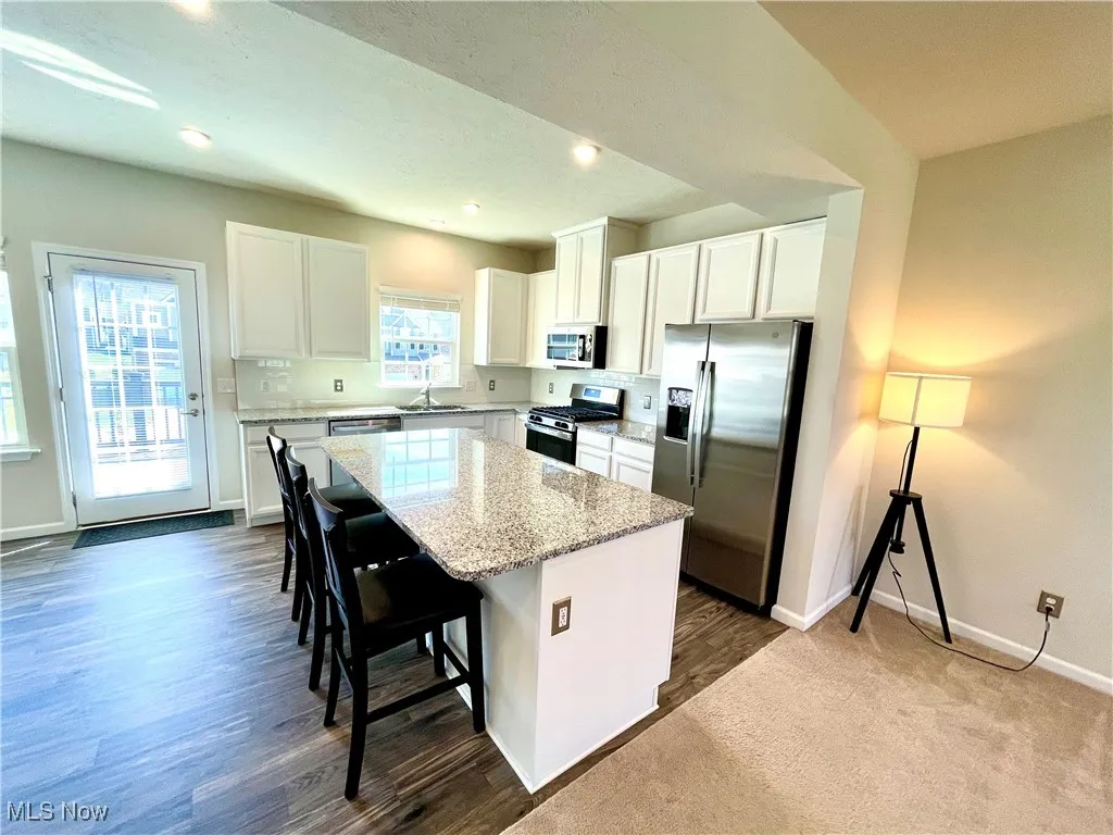 Kitchen featuring white cabinets, stainless steel appliances, light stone countertops, a kitchen island, and a breakfast bar area