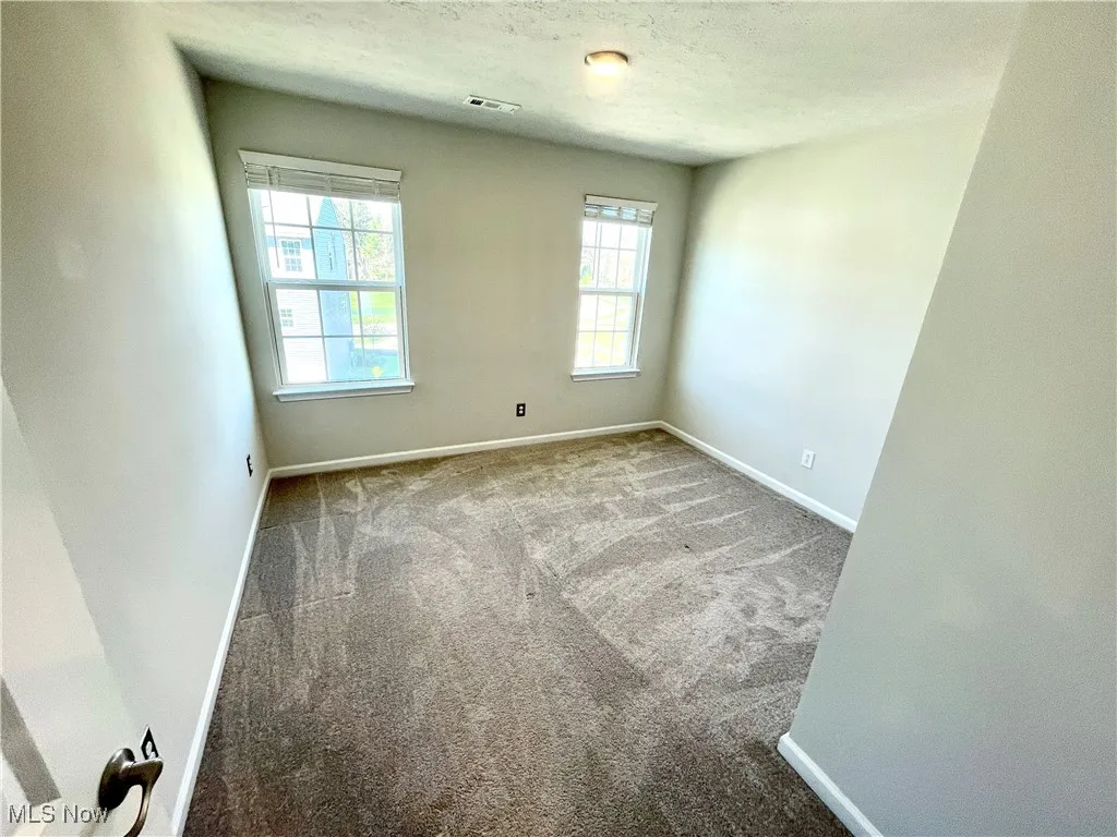 Empty room featuring a textured ceiling, carpet floors, visible vents, and baseboards