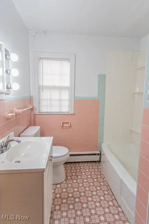 Full bath featuring a wainscoted wall, toilet, tile walls, a baseboard radiator, and tile patterned floors