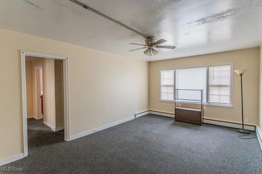 Unfurnished room featuring dark carpet, ceiling fan, a baseboard radiator, and baseboards