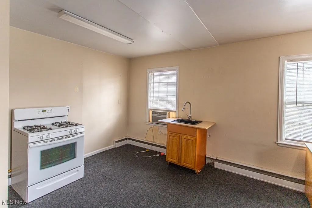 Kitchen featuring light countertops, a baseboard radiator, a sink, and white gas range oven