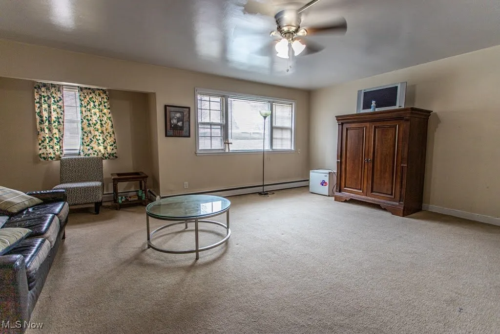 Living room featuring a baseboard heating unit, baseboards, light colored carpet, and a ceiling fan