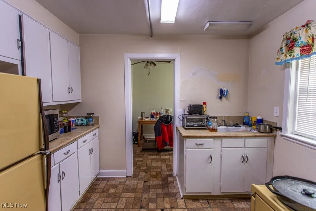 Kitchen with freestanding refrigerator, light countertops, stainless steel microwave, and white cabinets