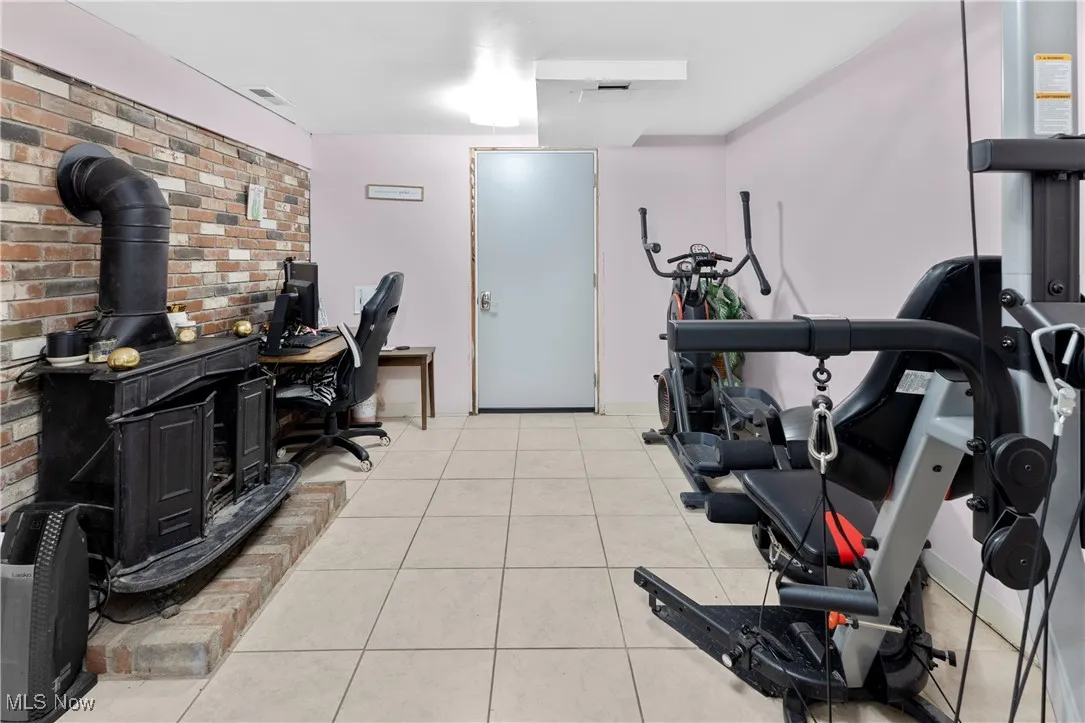 Exercise area with brick wall, light tile patterned flooring, a wood stove, and visible vents