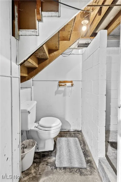 Bathroom with unfinished concrete floors, toilet, and concrete block wall