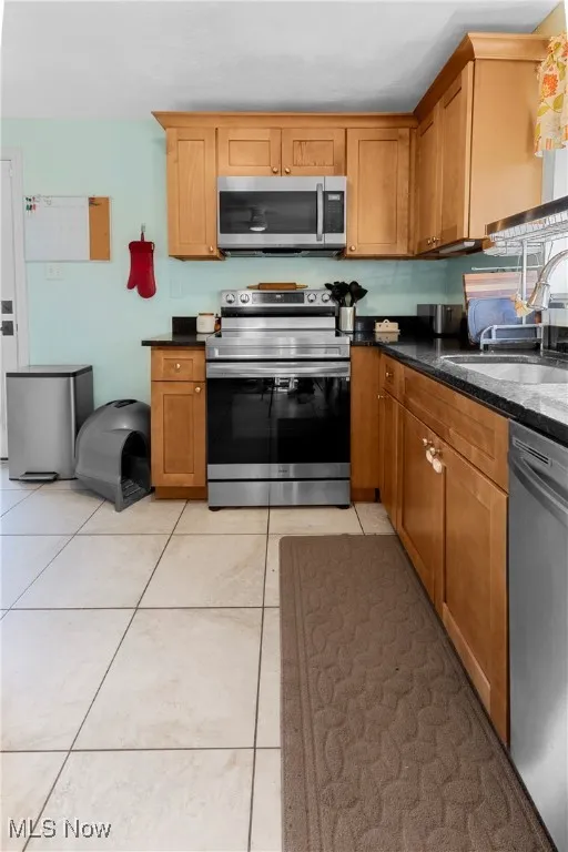 Kitchen featuring brown cabinets, appliances with stainless steel finishes, a sink, and light tile patterned flooring
