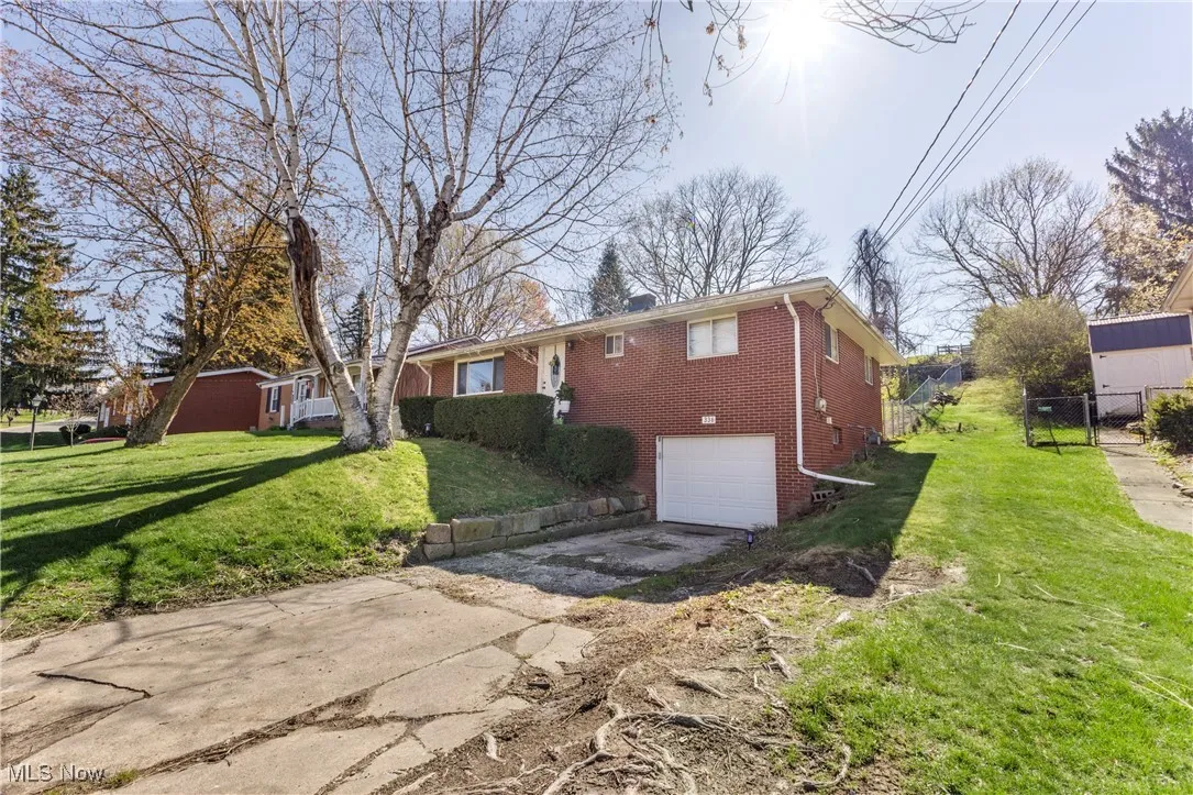 View of side of property with driveway, fence, brick siding, a garage, and a lawn