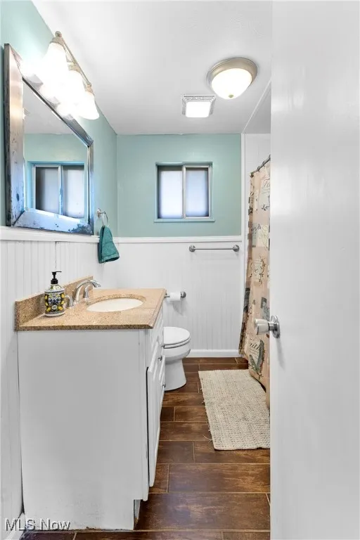 Bathroom with wood finished floors, vanity, a wainscoted wall, toilet, and a shower with shower curtain