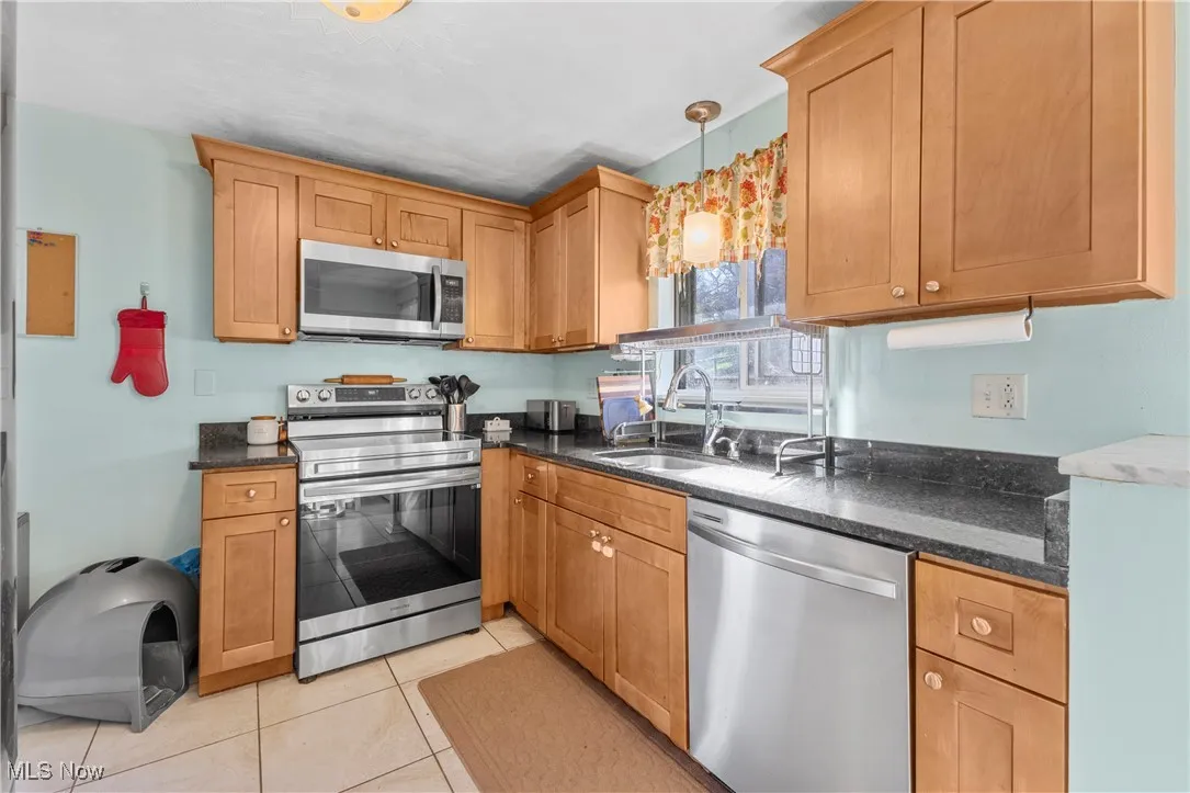 Kitchen with dark stone countertops, a sink, light tile patterned floors, pendant lighting, and appliances with stainless steel finishes