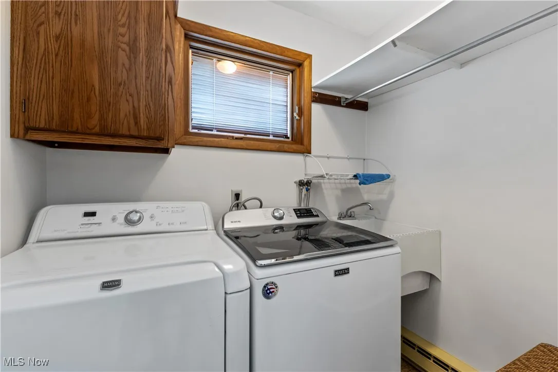 Clothes washing area featuring baseboard heating, separate washer and dryer, a sink, and cabinet space