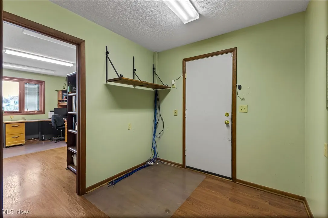 Garage entryway featuring baseboards, light wood-type flooring, and a textured ceiling
