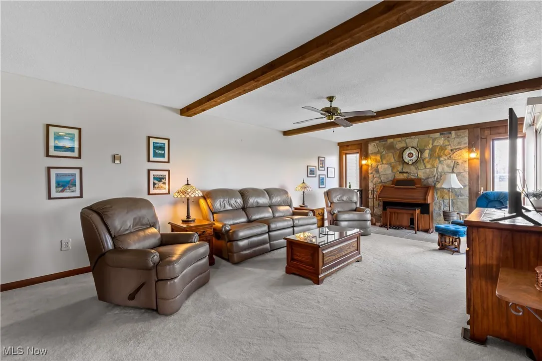 Carpeted living room with beamed ceiling, ceiling fan, baseboards, and a textured ceiling