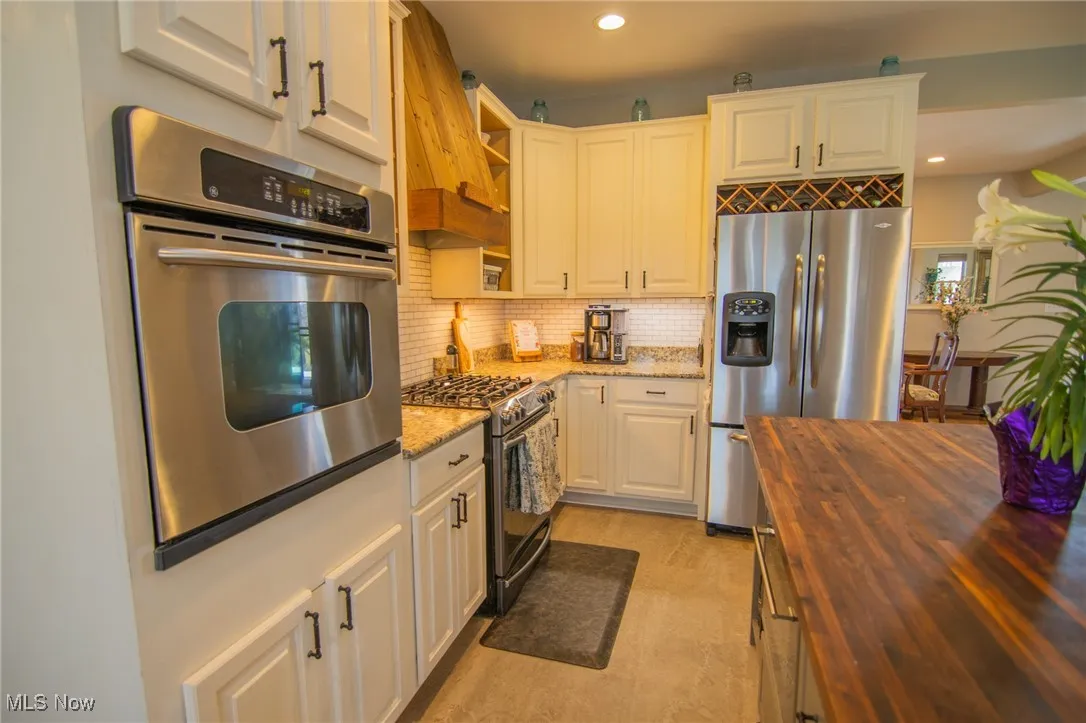 Kitchen with open shelves, wood counters, backsplash, appliances with stainless steel finishes, and recessed lighting