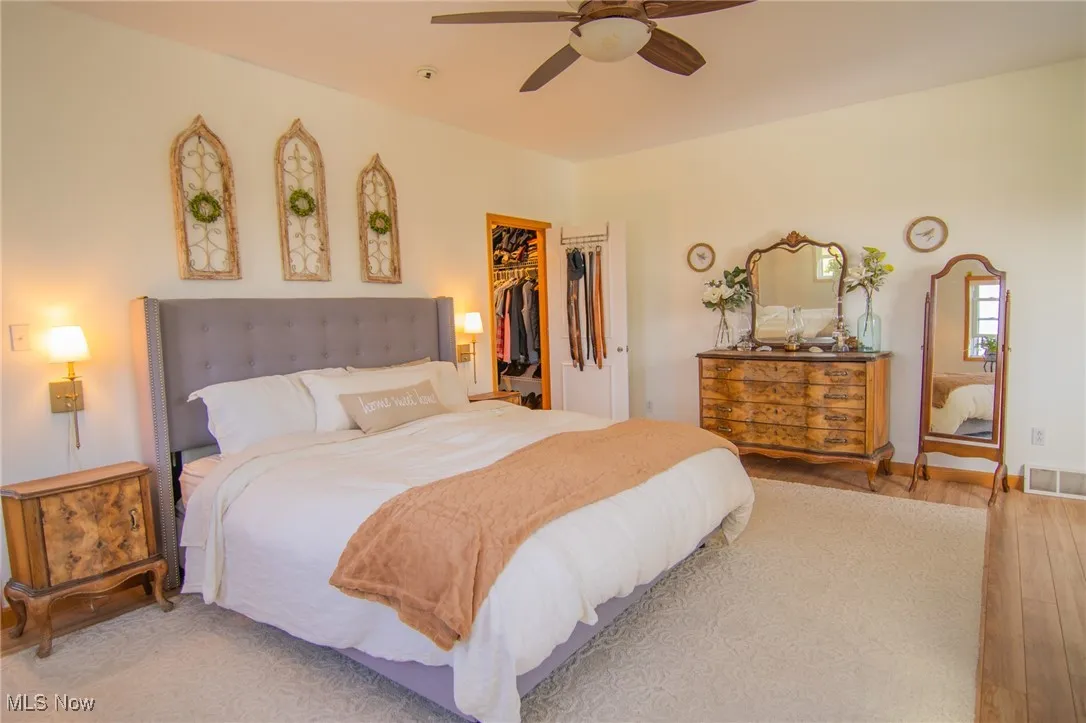 Bedroom with wood finished floors, visible vents, a ceiling fan, a walk in closet, and a closet