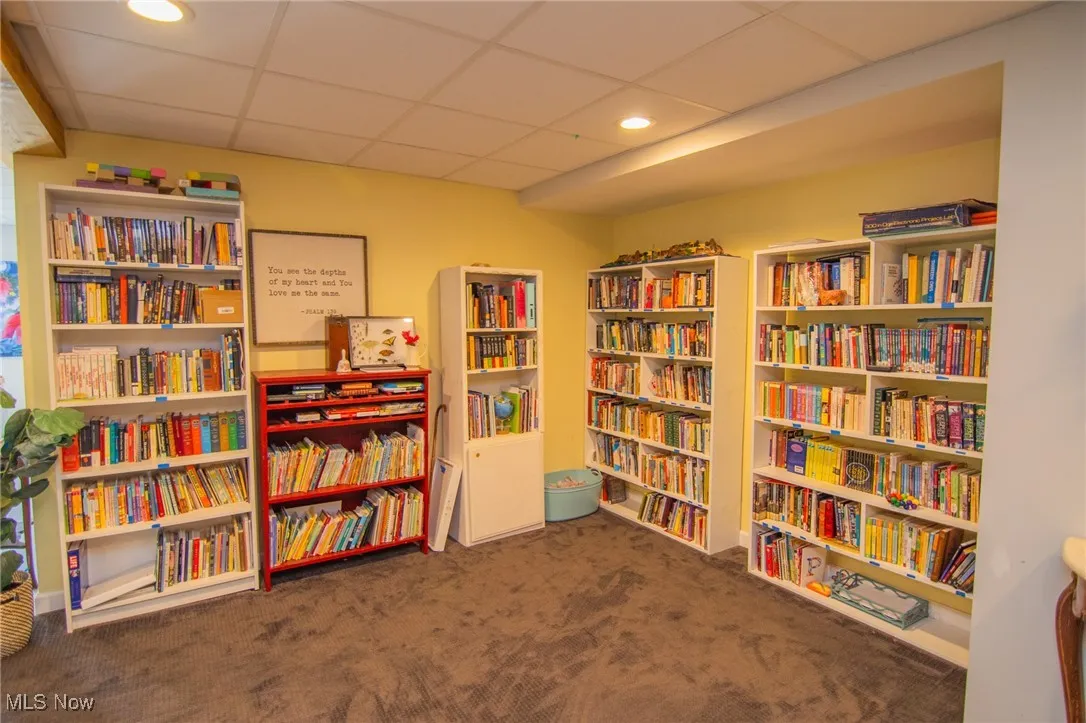 Sitting room with bookshelves, a paneled ceiling, carpet flooring, and recessed lighting