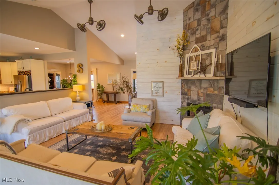 Living area featuring wooden walls, high vaulted ceiling, light wood-style floors, and a fireplace