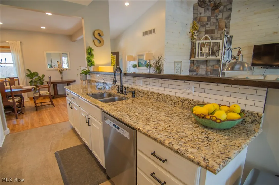 Kitchen featuring stainless steel dishwasher, tasteful backsplash, a sink, light stone countertops, and visible vents
