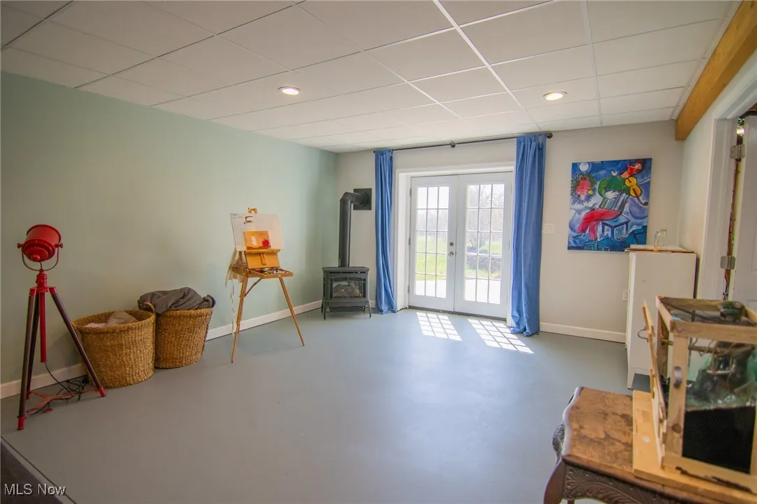 Misc room with a drop ceiling, a wood stove, french doors, concrete flooring, and baseboards
