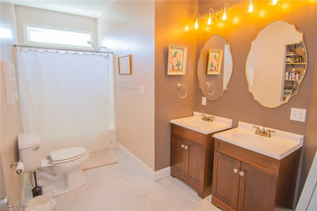Full bath with two vanities, a shower with curtain, a sink, and toilet