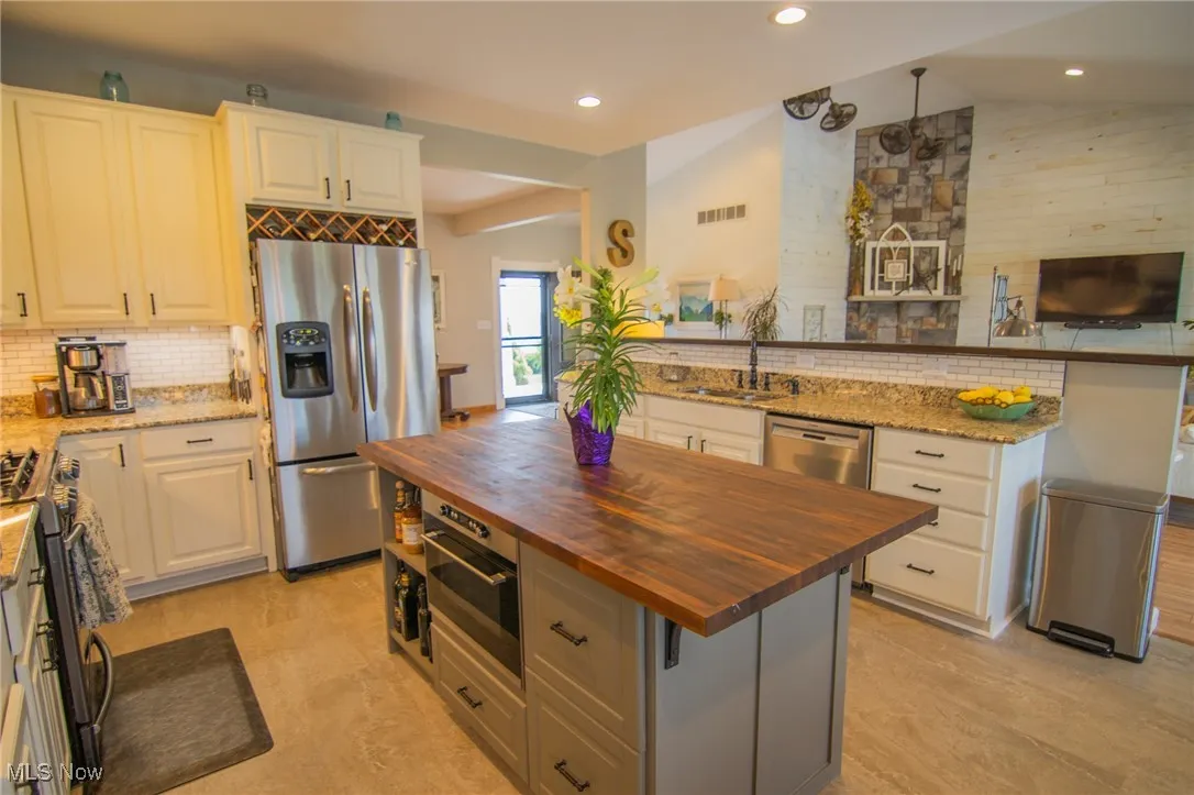 Kitchen with backsplash, vaulted ceiling, a sink, butcher block counters, and appliances with stainless steel finishes