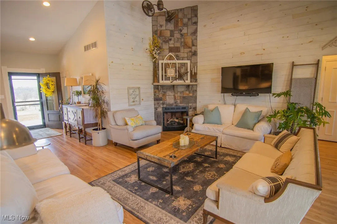 Living room with high vaulted ceiling, wood finished floors, a fireplace, visible vents, and recessed lighting