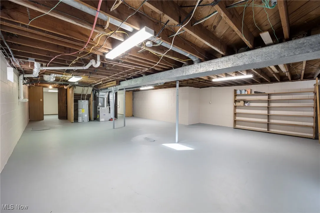Unfinished below grade area featuring concrete block wall, heating unit, and water heater