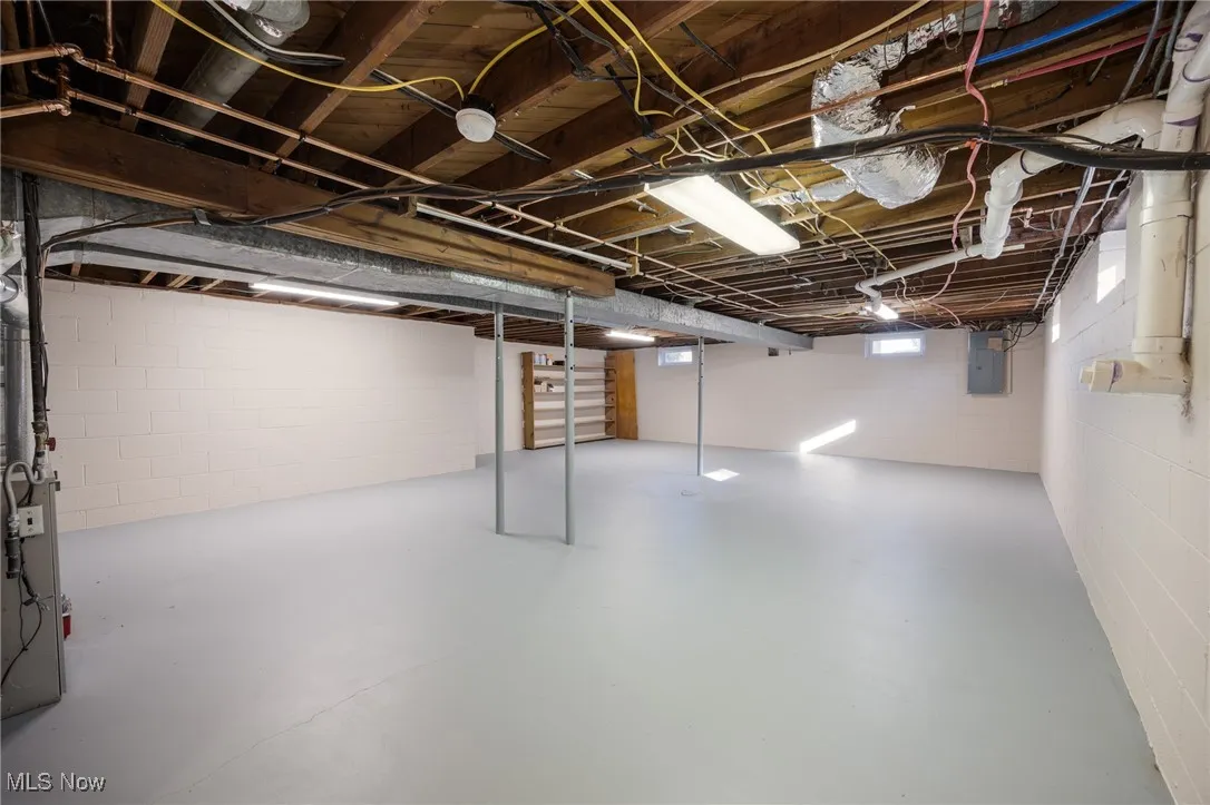 Unfinished basement featuring concrete block wall and electric panel