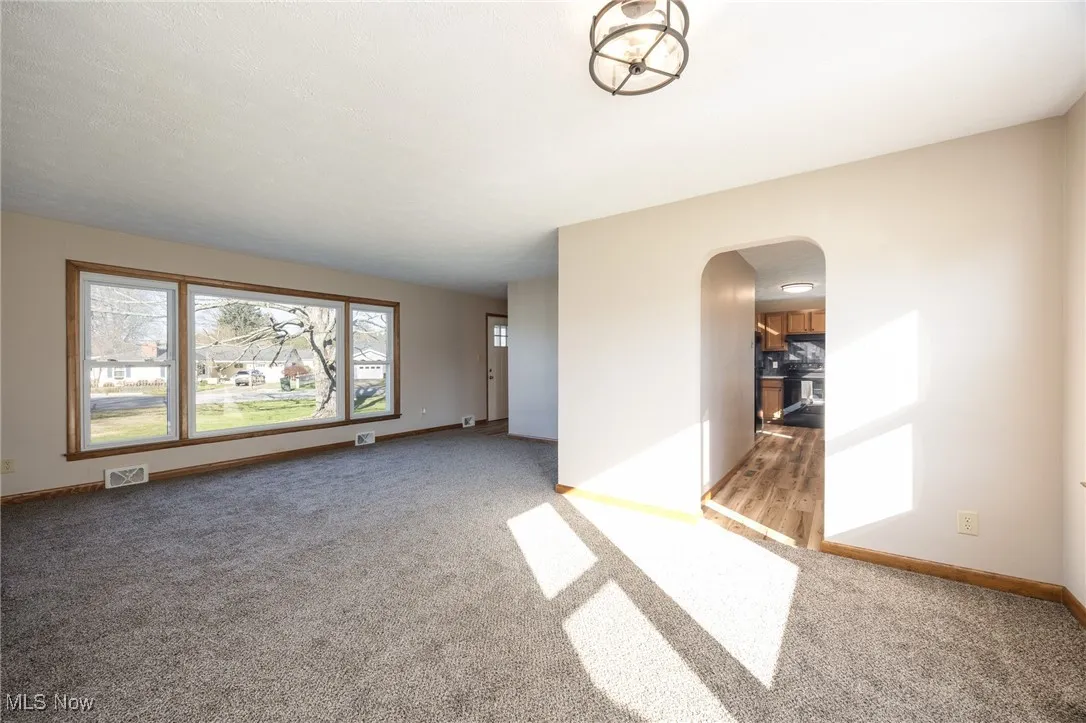 Dining room view into living area, featuring light colored carpet, arched walkways, and baseboards
