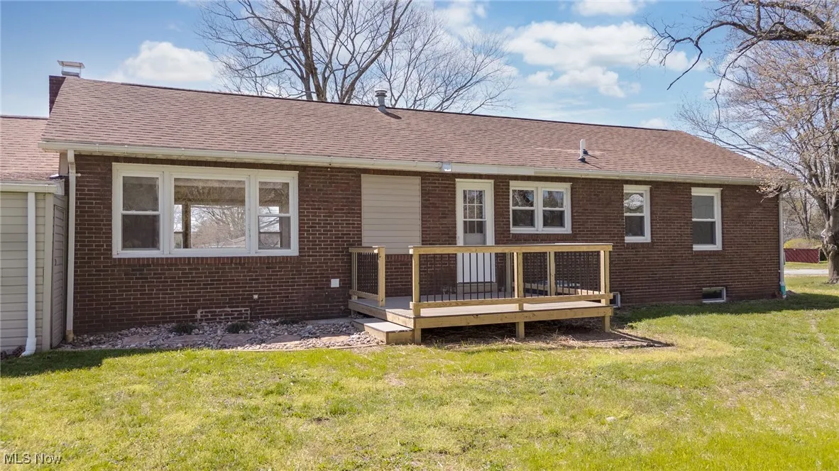 Back of house with brick siding, a yard, a shingled roof, and a deck
