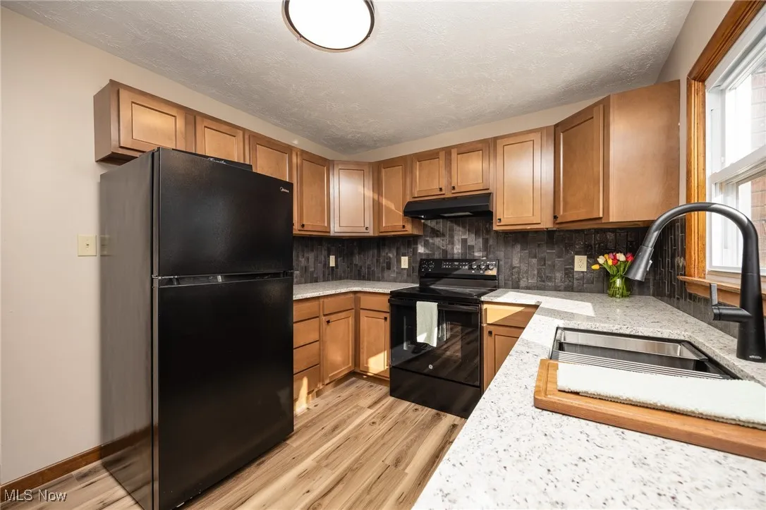 Kitchen featuring light wood-type flooring, under cabinet range hood, a sink, and black appliances