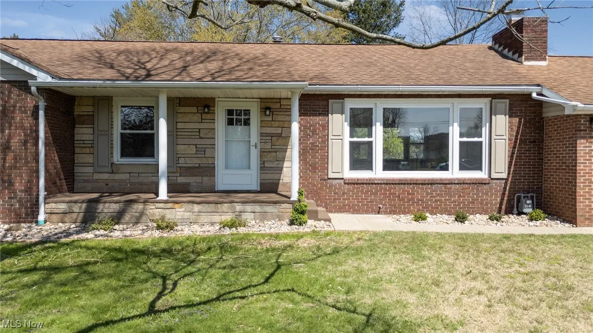 View of front of house with a chimney, brick siding, a porch, roof with shingles, and a front yard