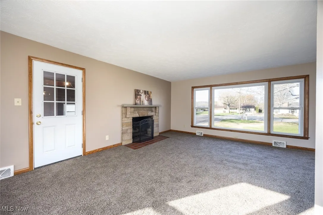 Unfurnished living room with a fireplace, baseboards, visible vents, and carpet
