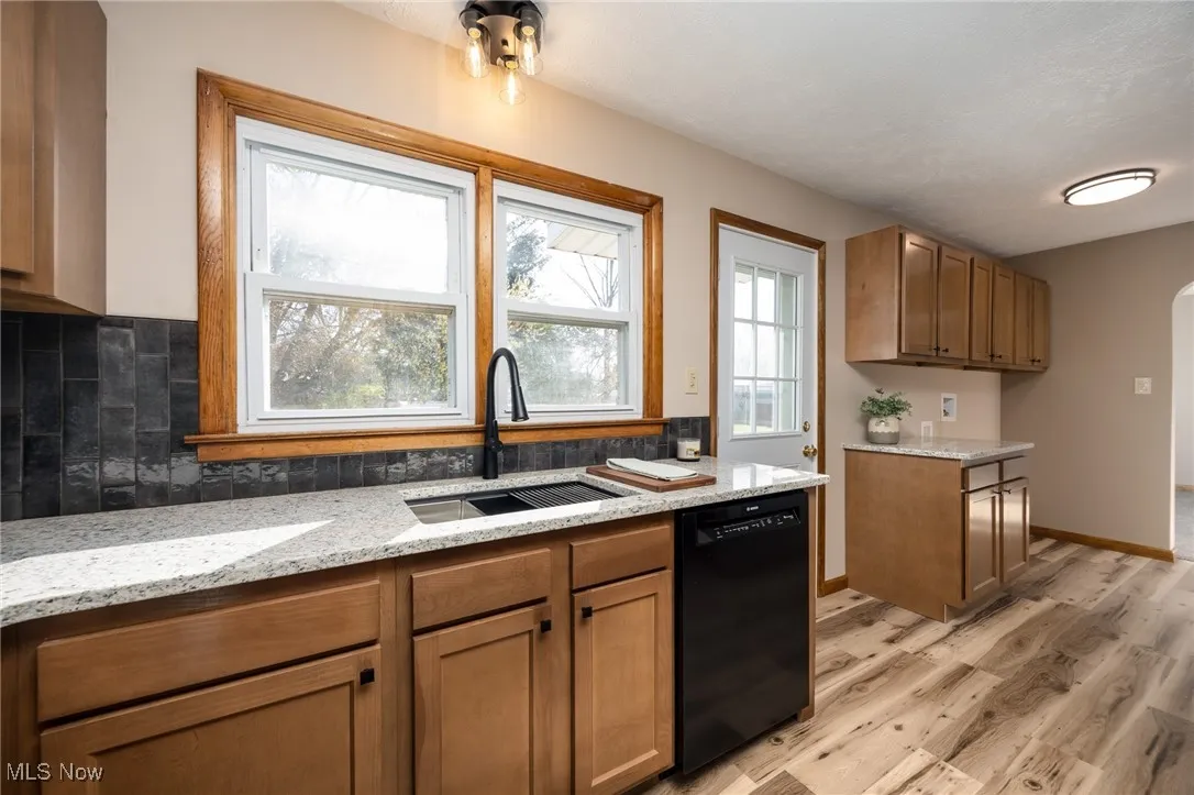 Kitchen featuring a sink, decorative backsplash, light wood-type vinyl flooring, light granite countertops, and black dishwasher. Exit to back deck.