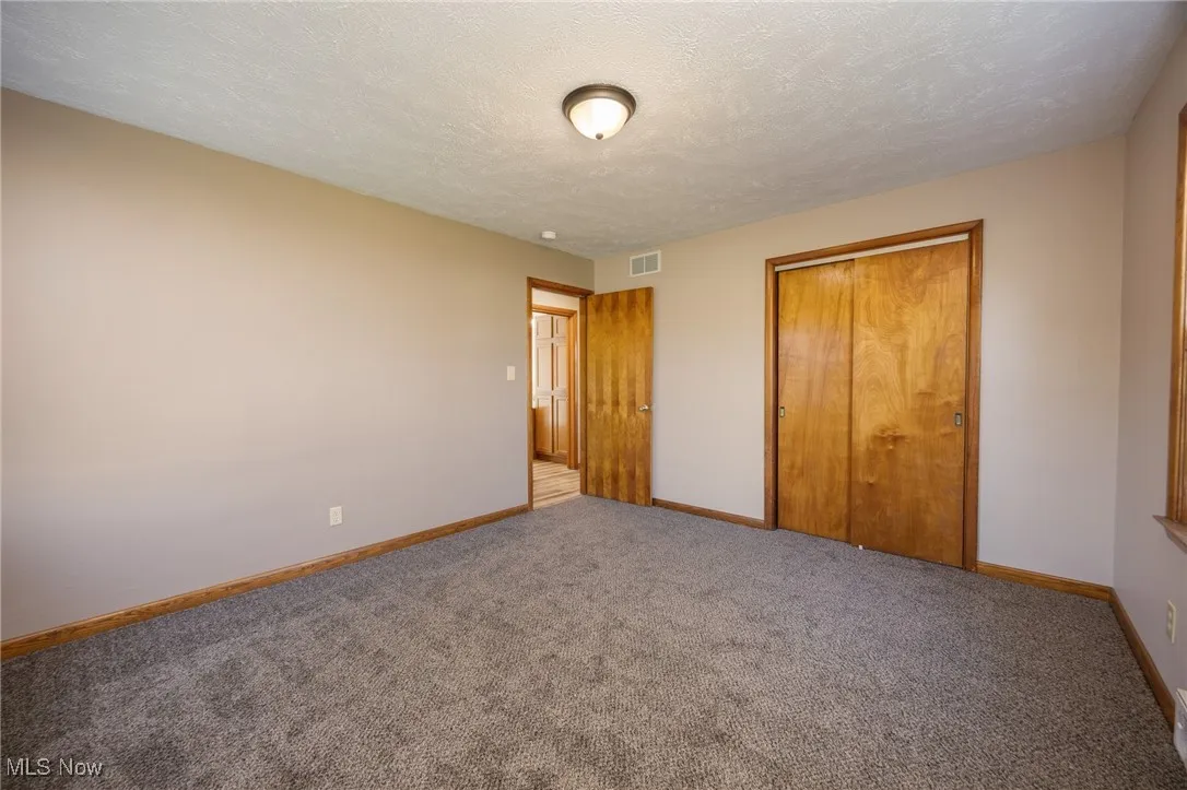 Unfurnished bedroom featuring a textured ceiling, baseboards, visible vents, carpet, and a closet