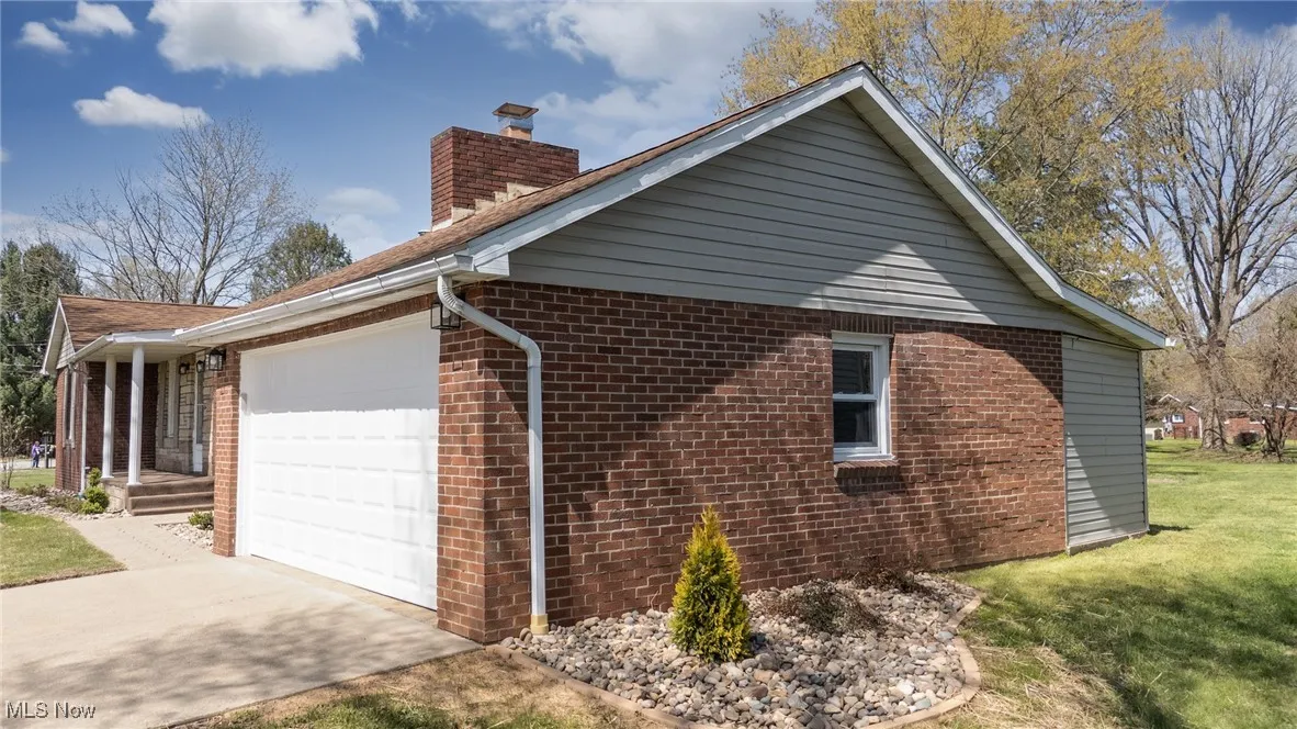 View of home's exterior featuring a chimney, a yard, an attached garage, driveway, and brick siding
