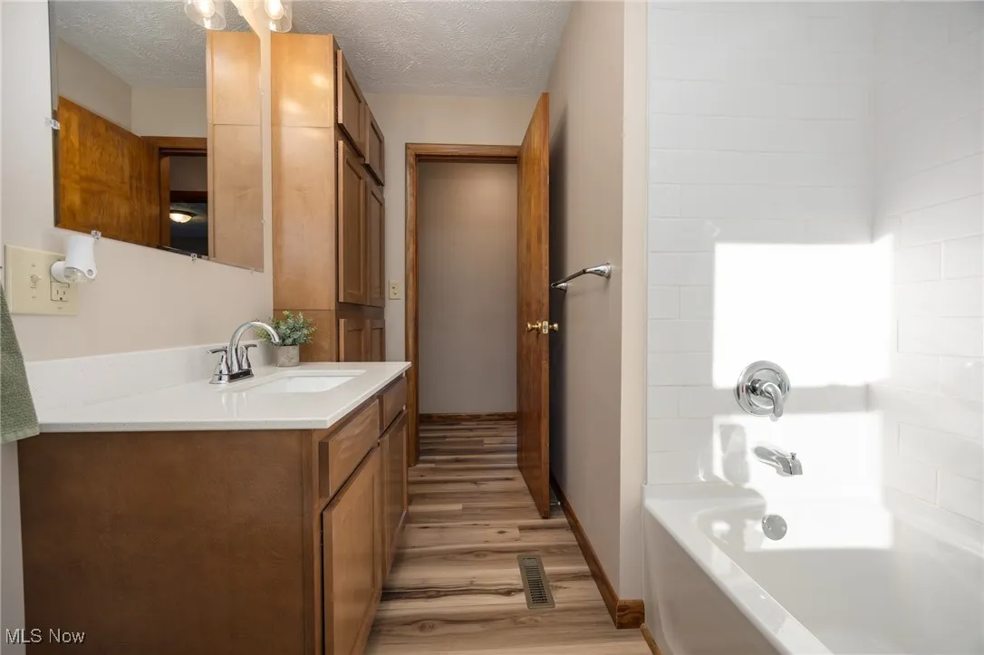 Full bath with shower / bathtub combination, visible vents, baseboards, wood look LVP floors, and vanity