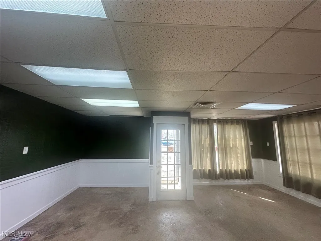 Empty room with concrete floors, a paneled ceiling, visible vents, and a wainscoted wall